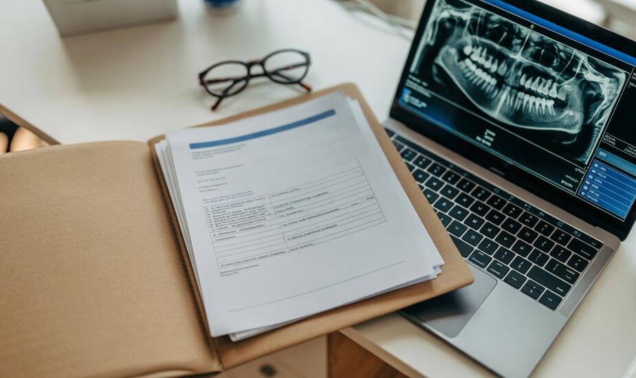 Unreported CBCT scans medicolegal risk - dental practice desk with radiology report and CBCT scan on laptop